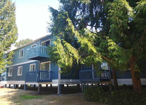 A blue house with a deck and trees in front.