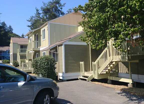 A silver car is parked in front of a two-story house with a garage and a staircase leading to the front door.