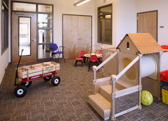 A child's play area with a wooden dollhouse, a wagon, and a ball.