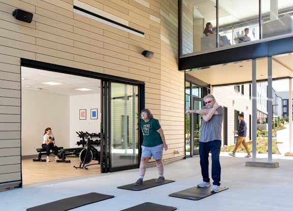 A man and a woman are exercising in a gym with wooden walls and ceiling.
