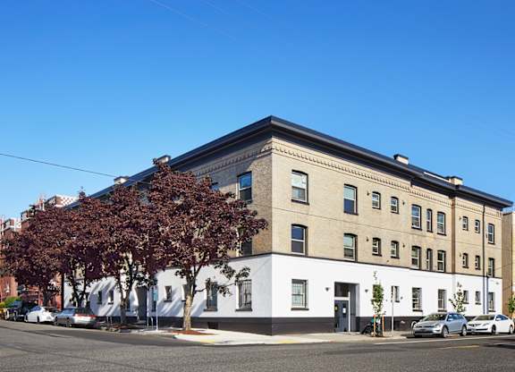 A white and beige building with a black roof and a tree with red leaves in front.