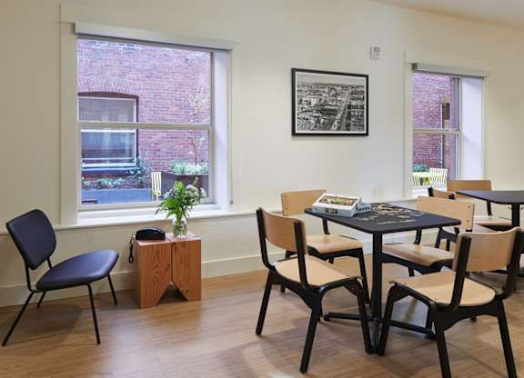 A black chair sits in front of a window in a room with a table and chairs.