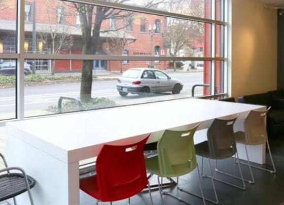 A white table with red and green chairs in front of a window with a view of a street.