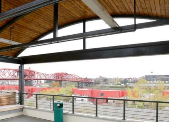A balcony with a green trash can and a view of a bridge.