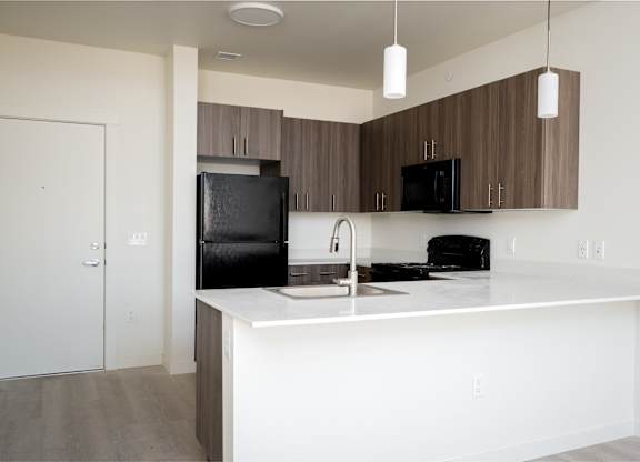 A kitchen with a black fridge and microwave, brown cabinets, and a white countertop.