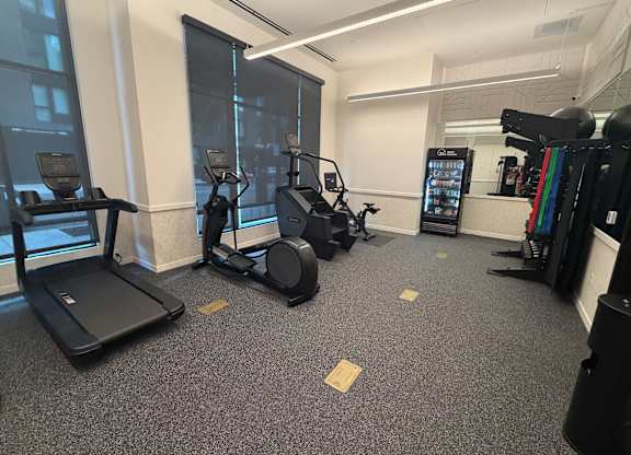 A gym with treadmills, elliptical machines, and a weight rack.