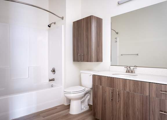 A white toilet sits next to a white bathtub in a bathroom with wooden cabinets.