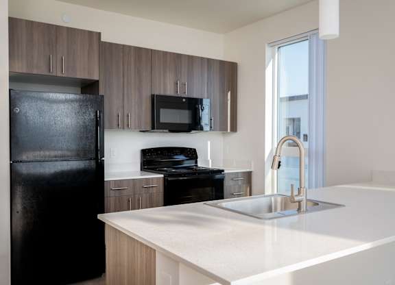 A black fridge stands next to a white counter in a modern kitchen.