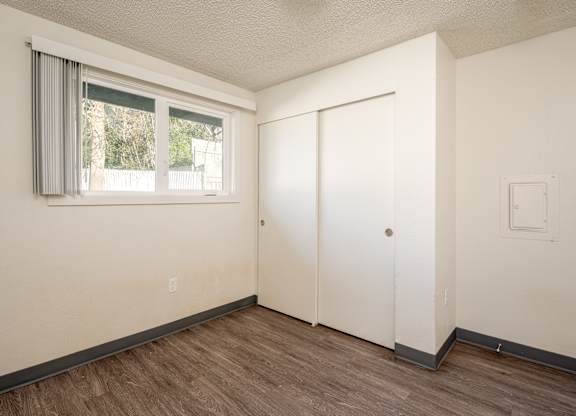A room with a white door, a window with grey curtains, and a light switch on the wall.