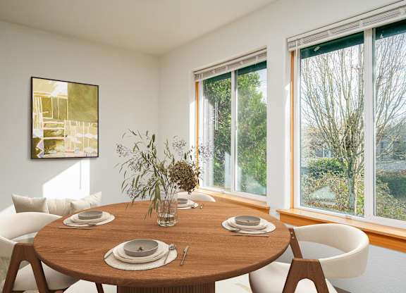 A dining table set with plates and cutlery is in front of a window with a view of trees.