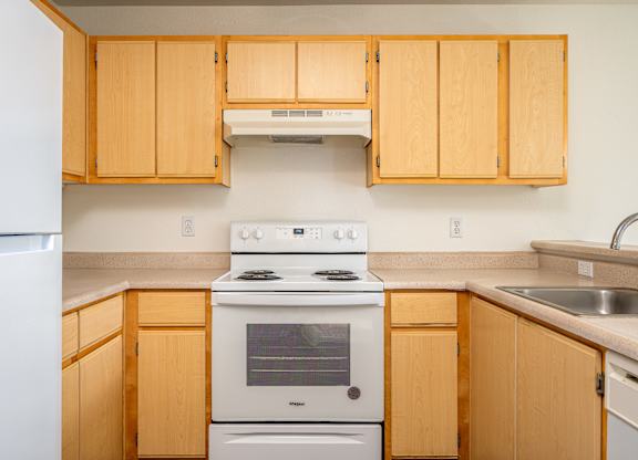 A kitchen with wooden cabinets and a white stove top oven.