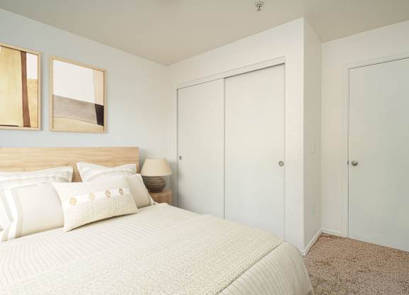 A bedroom with a bed, two pillows, a nightstand with a lamp, and two pictures on the wall.