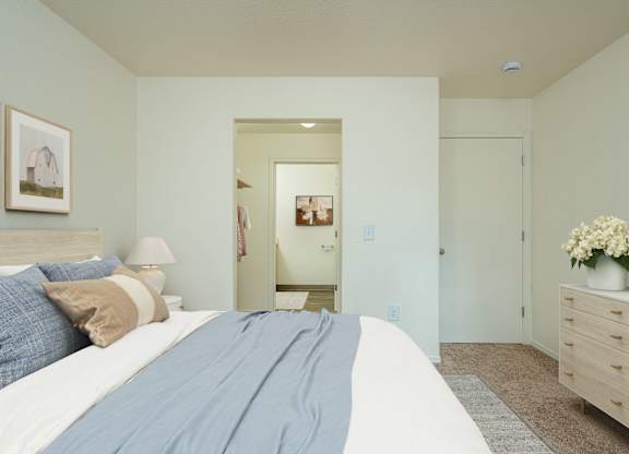 A bedroom with a large bed and a dresser with a vase of flowers on top.