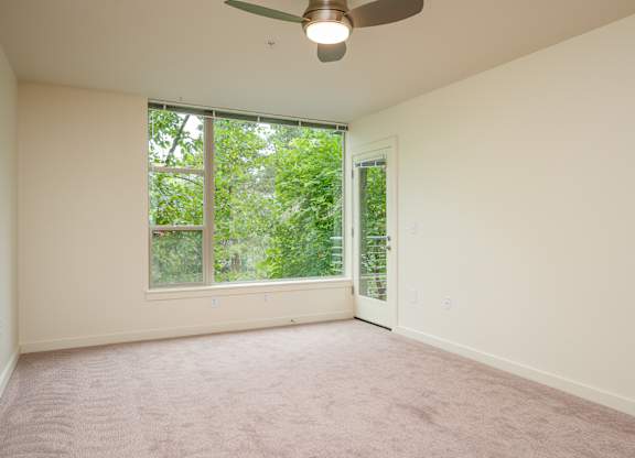 A room with a ceiling fan and a window overlooking a green area.