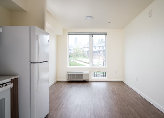 an empty living room with a refrigerator and a window