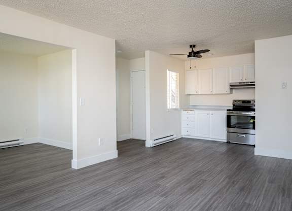 A room with a ceiling fan and a kitchen area in the background.