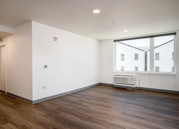 a living room with white walls and wood flooring and a large window