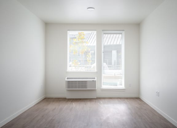 an empty room with two windows and wood floors