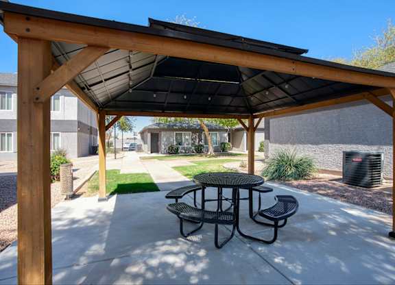 A wooden pergola with a black canopy is over a picnic table.