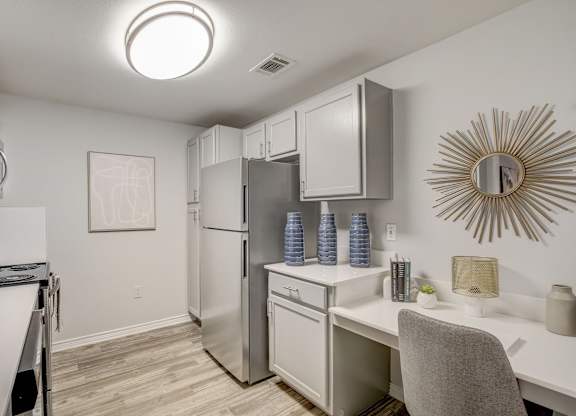 A kitchen with a refrigerator, microwave, and a desk with a chair.