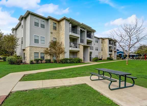 A large apartment complex with a green lawn and a picnic table in front.