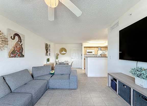 A living room with a grey couch and a white ceiling fan.