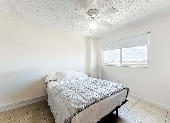 A bedroom with a bed, a ceiling fan, and a window with blinds.