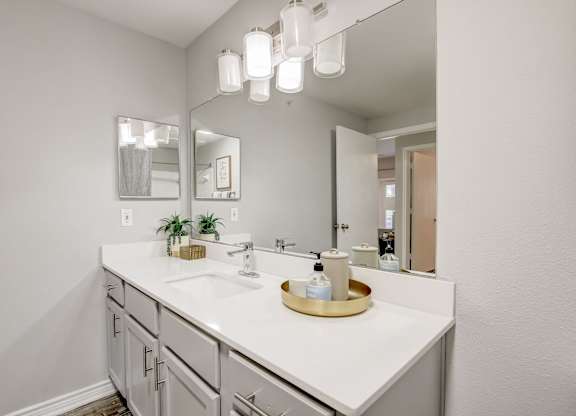 A bathroom with a white counter top and a mirror above it.