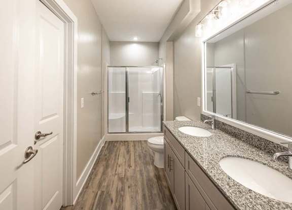 A bathroom with a toilet, sink, mirror, and shower at Foxwood Apartments, Raleigh-Durham, NC