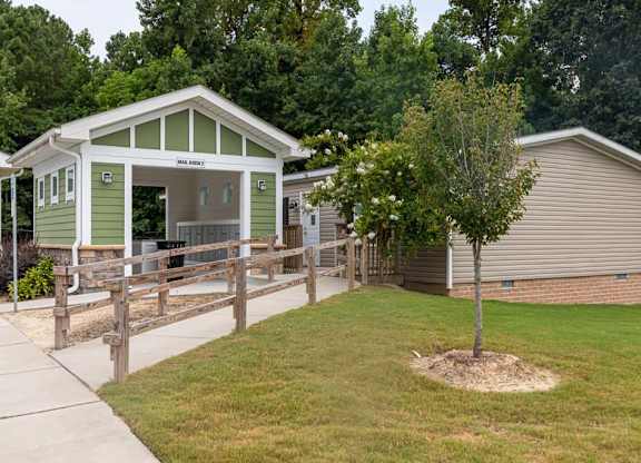 A green and white building with a porch and a tree in front of a beige building at Foxwood Apartments, Raleigh-Durham, North Carolina