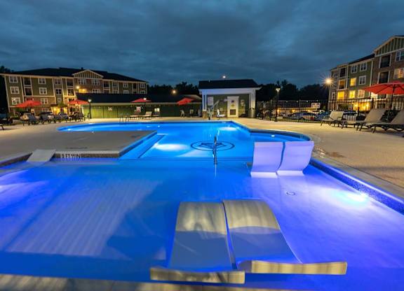 A large outdoor swimming pool lit up with blue lights at night. at Foxwood Apartments, Raleigh-Durham