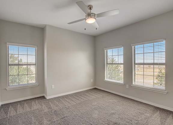 A room with a ceiling fan and two windows.