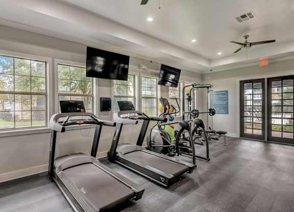 A spacious gym with treadmills, elliptical machines, and a fan.