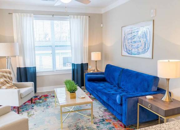 A blue couch sits in a living room with a white chair and a small table with a plant on it at Foxwood Apartments, North Carolina