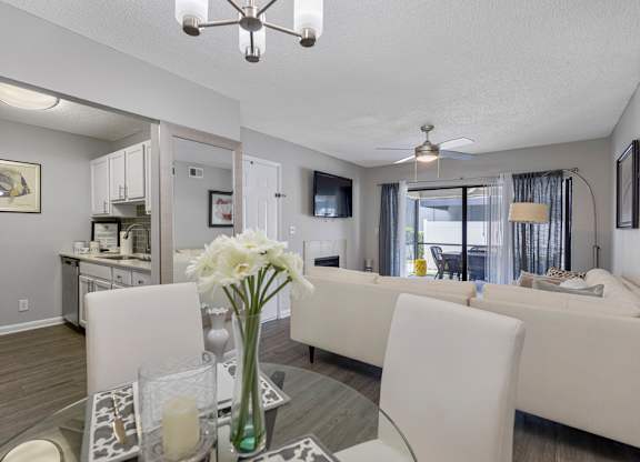 A living room with a white couch and a glass table with a vase of white flowers on it.