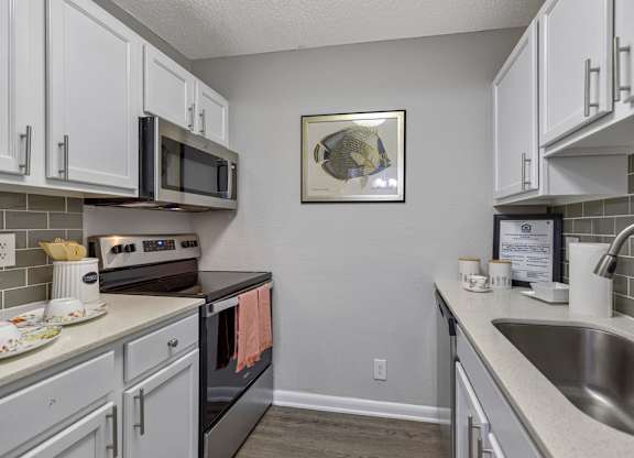 A kitchen with white cabinets and a black microwave above the stove.