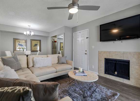 A living room with a white couch and a television mounted on the wall.