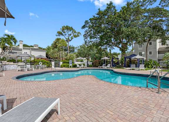 A pool surrounded by a brick patio and trees.