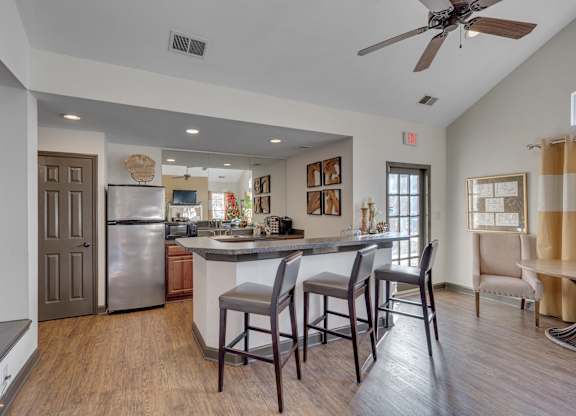 A kitchen with a refrigerator, sink, and bar stools.