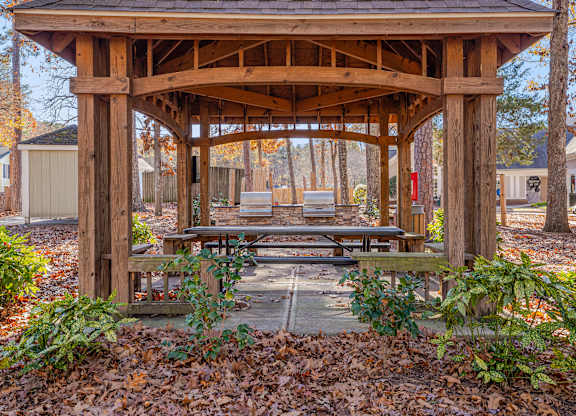 A wooden gazebo with a roof and a bench in front of it.