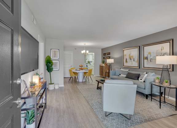 A well-lit living room with a grey sofa and a dining table set for four.
