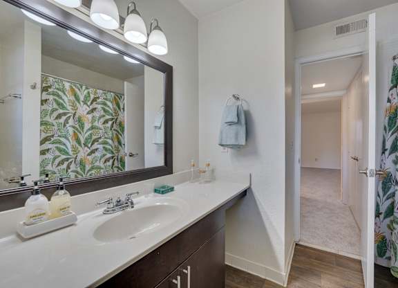 A bathroom with a floral shower curtain and a mirror above a double sink.
