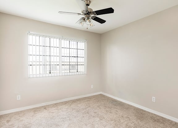 A room with a ceiling fan and a window with blinds.