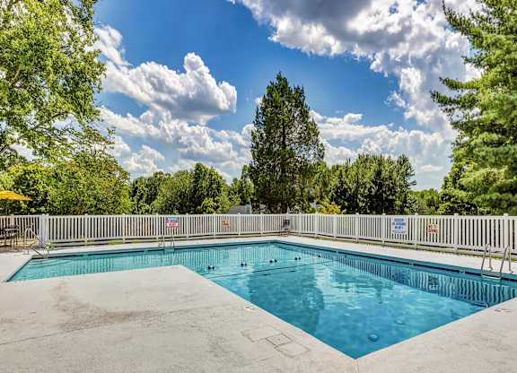 A large outdoor swimming pool surrounded by a white fence and trees. at Brandemere Apartment Homes, North Carolina, 27106