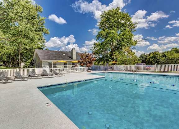 A large swimming pool surrounded by trees and a house in the background. at Brandemere Apartment Homes, North Carolina