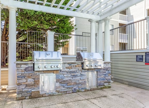 an outdoor kitchen with two grills and a stone wall at Bridges at Mallard Creek Apartment Homes, North Carolina, 28269