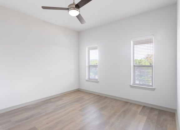 an empty room with a ceiling fan and two windows