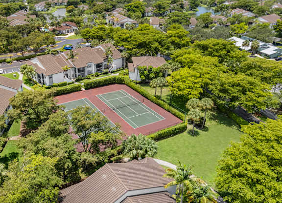 A tennis court is surrounded by apartments and trees.