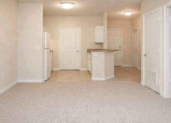 a carpeted living room with a view into the tiled kitchen