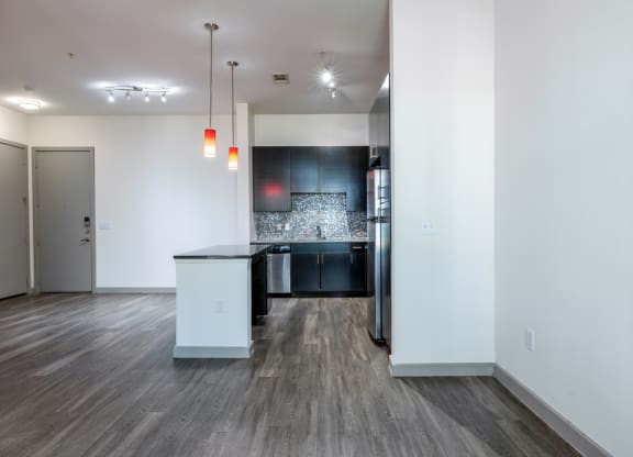 the living room and kitchen of an apartment with white walls and wood flooring